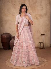 Front view of a model in a blush pink net lehenga with silver sequin embroidery, stitched V-neck blouse and net dupatta draped over one shoulder