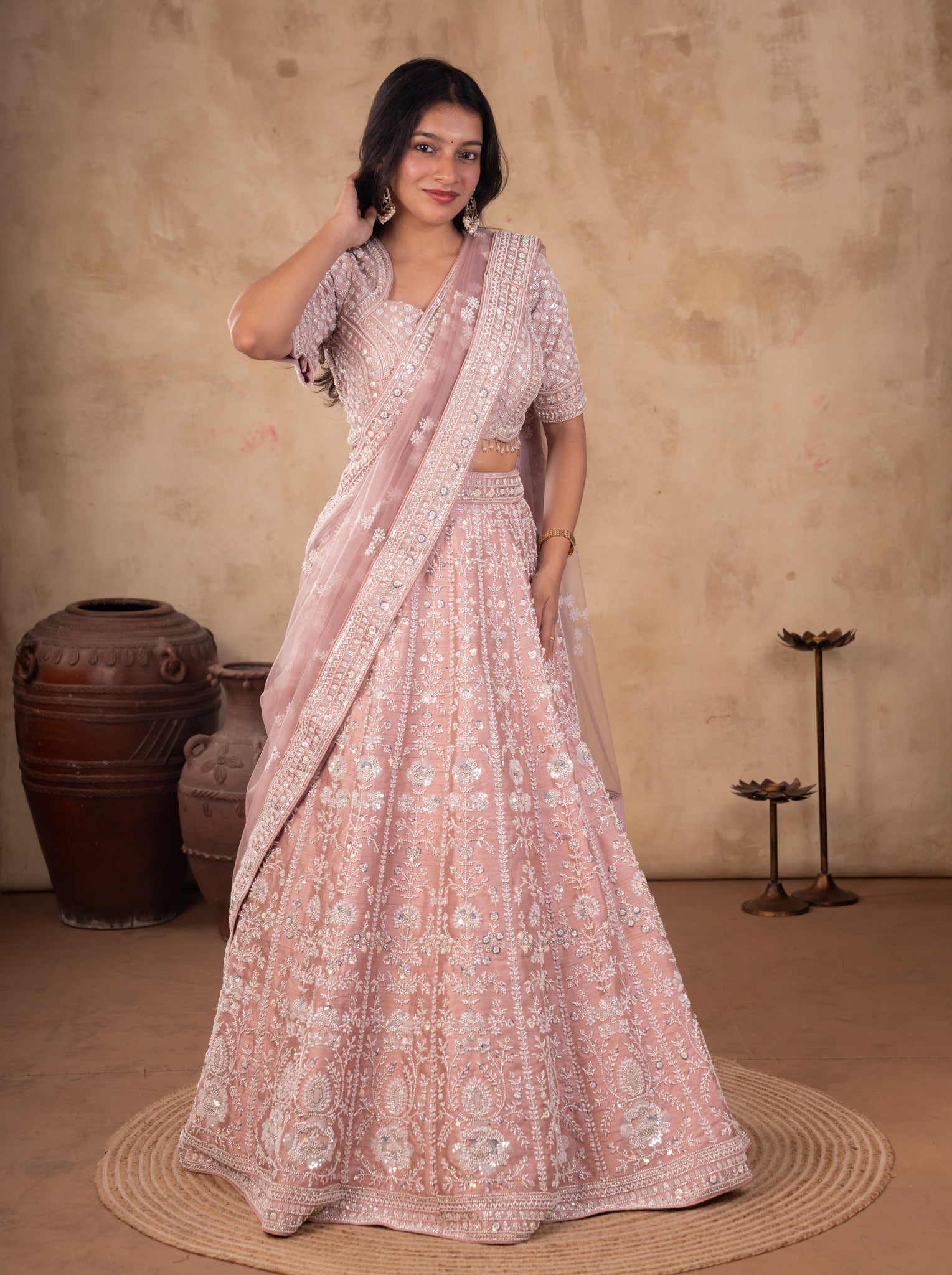Model adjusting her earring in a blush pink embroidered net lehenga with a stitched blouse and draped net dupatta