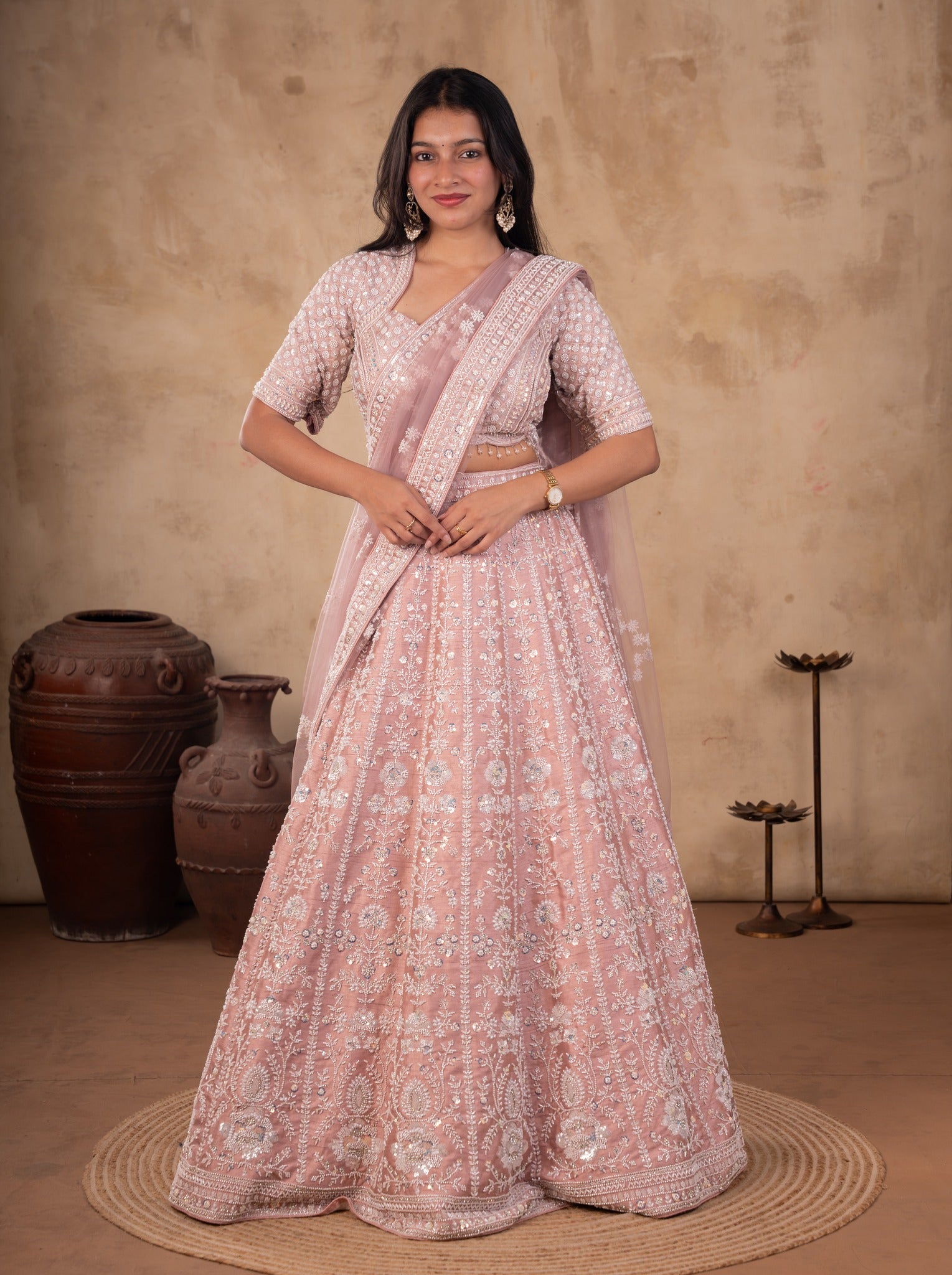 Full-length front view of a blush pink net lehenga set with sequin and thread embroidery and a dupatta pinned over the shoulder