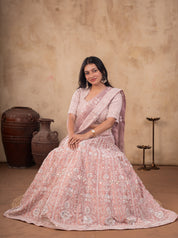 Model seated on a stool in a blush pink net lehenga set, the flared embroidered skirt spread around her