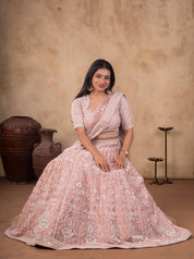 Seated pose in a blush pink embroidered net lehenga with stitched blouse and draped dupatta