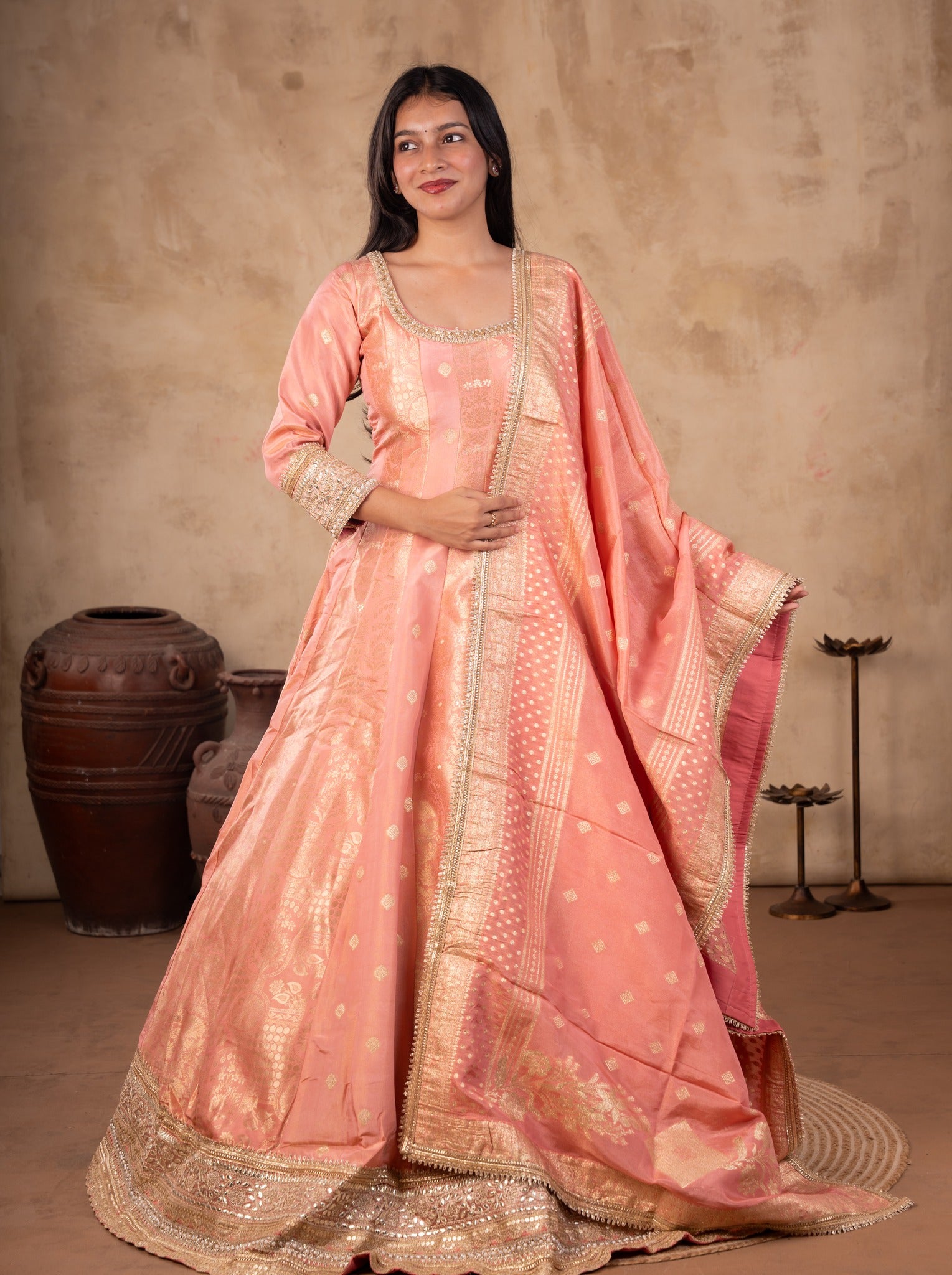 Model in a blush pink raw silk Anarkali set holding the gold-bordered dupatta, showing the flared skirt and gold hem