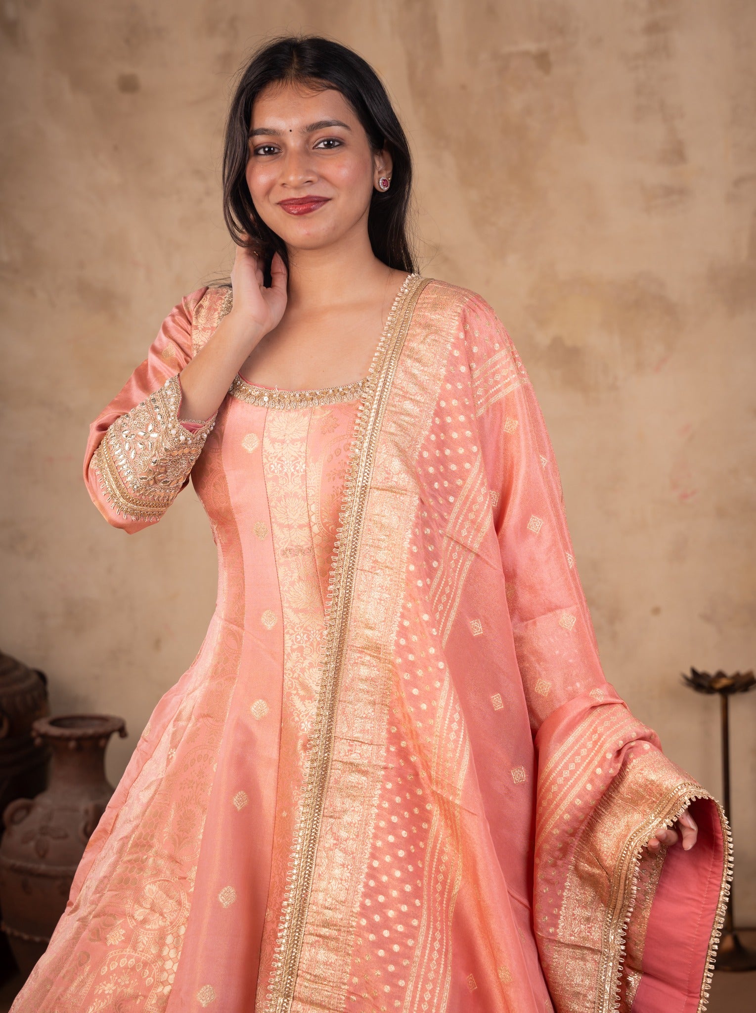 Half-length view of a blush pink raw silk Anarkali with an embellished neckline, gold motifs and a bordered dupatta