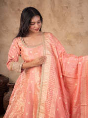 Model smiling in a blush pink raw silk Anarkali with embellished neckline, holding the dupatta out to the side