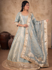 Front view of a model in a pale blue raw silk Anarkali with gold motifs, an ornate gold hem and a dotted dupatta with a wide gold border