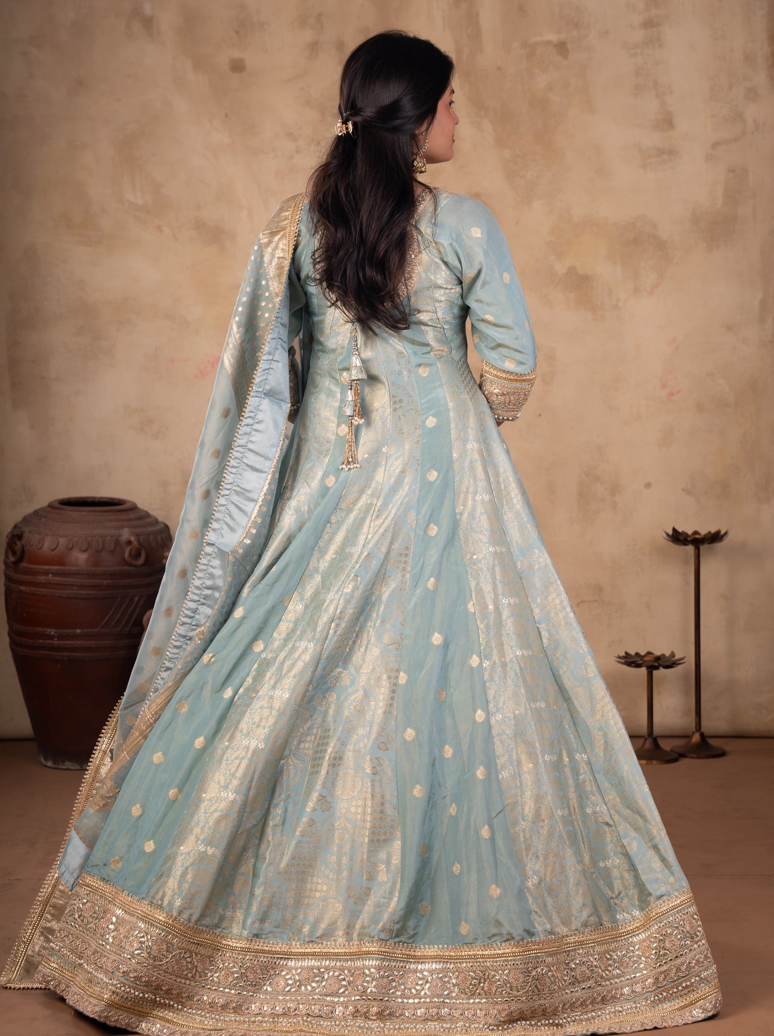 Back view of a pale blue raw silk Anarkali showing the flared skirt, gold hem and draped dupatta