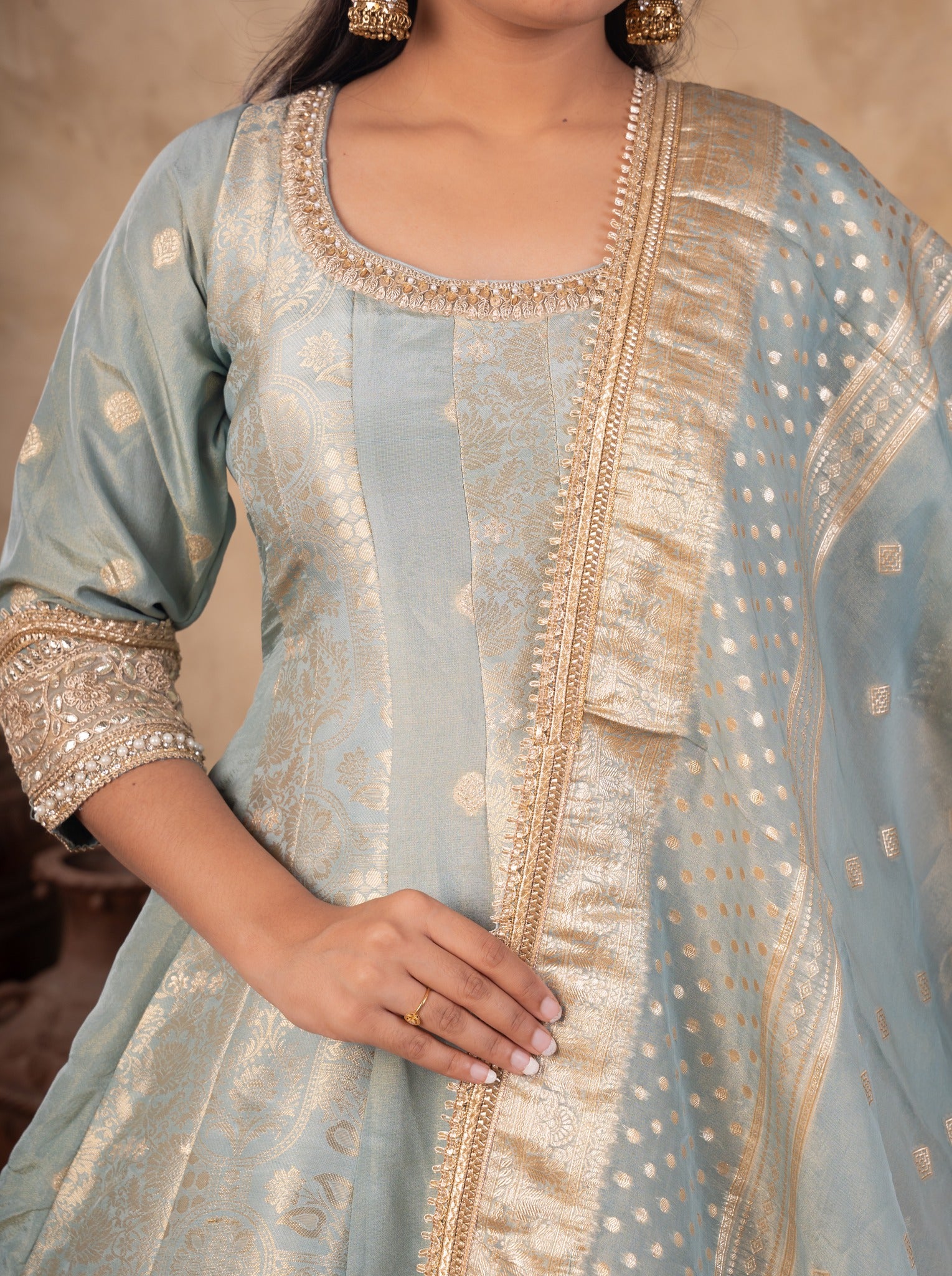 Half-length view of a pale blue raw silk Anarkali with an embellished neckline and gold-bordered dotted dupatta