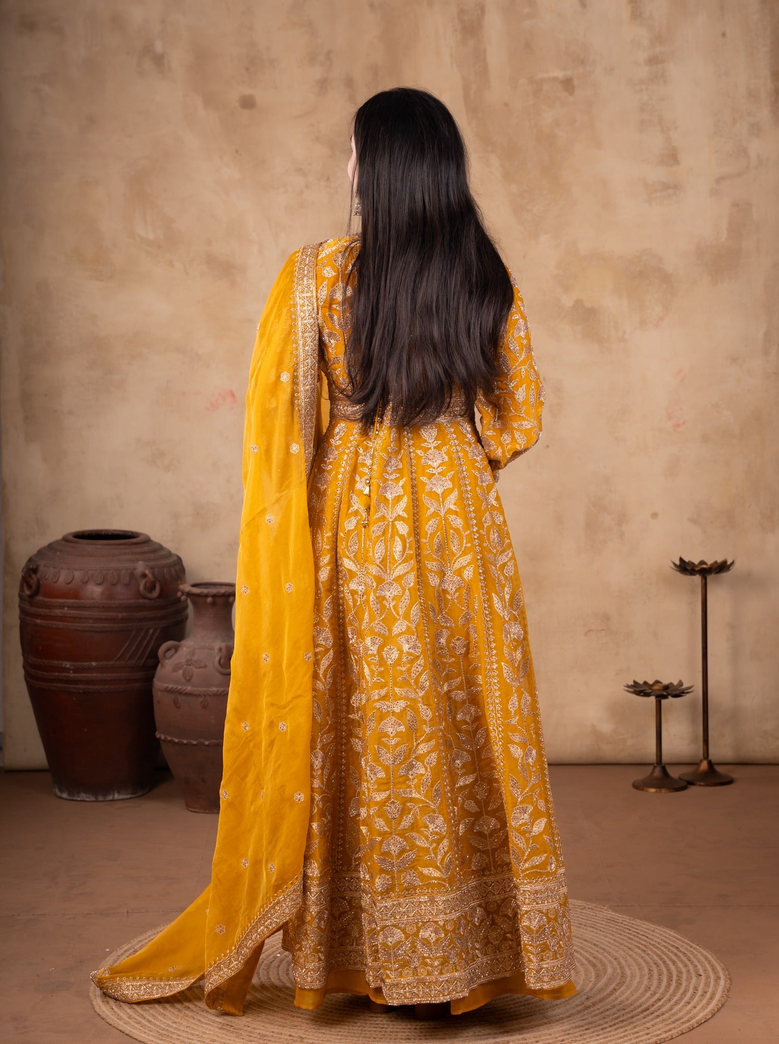 Back view of a mustard tissue Anarkali suit showing the flared skirt and the dupatta falling behind