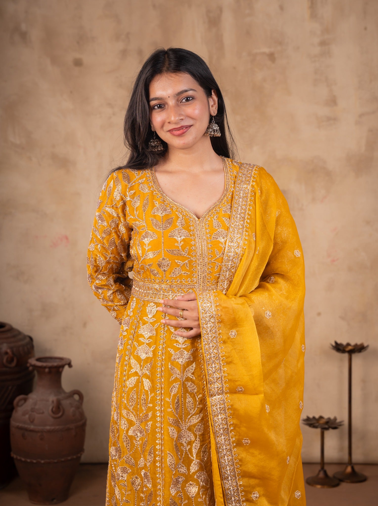 Model smiling in a mustard tissue Anarkali suit with an embroidered V-neck yoke and matching dupatta