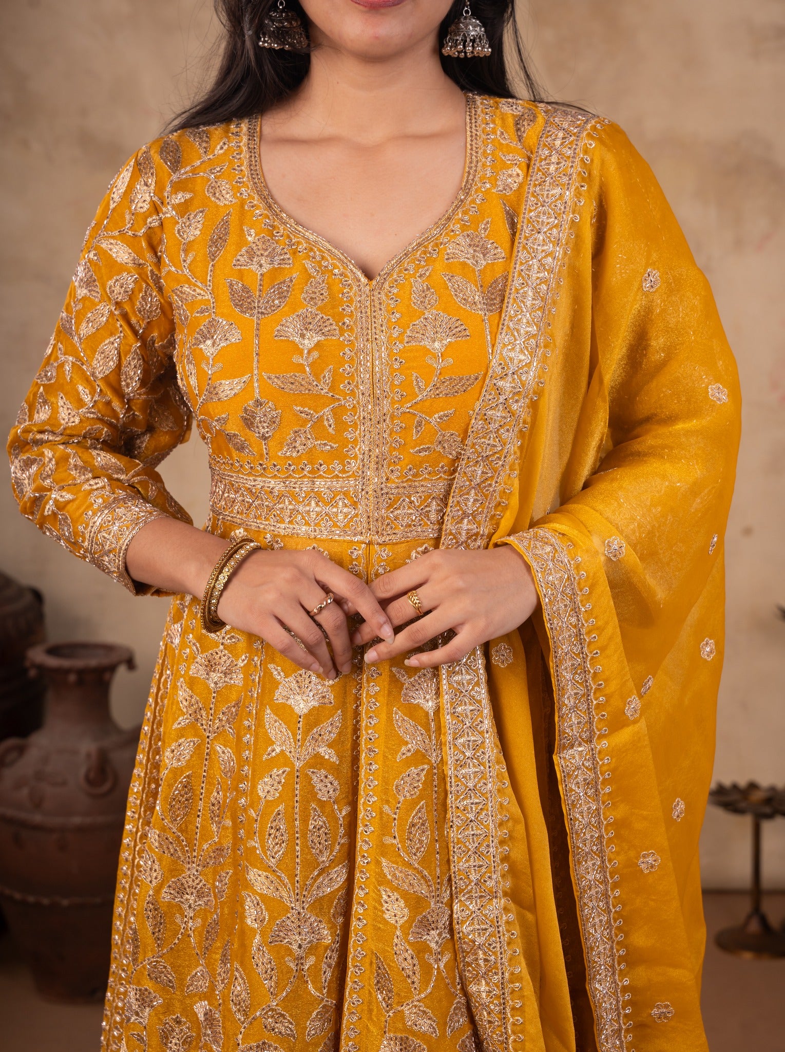 Close-up of the floral-embroidered bodice and waistband of a mustard tissue Anarkali with the bordered dupatta