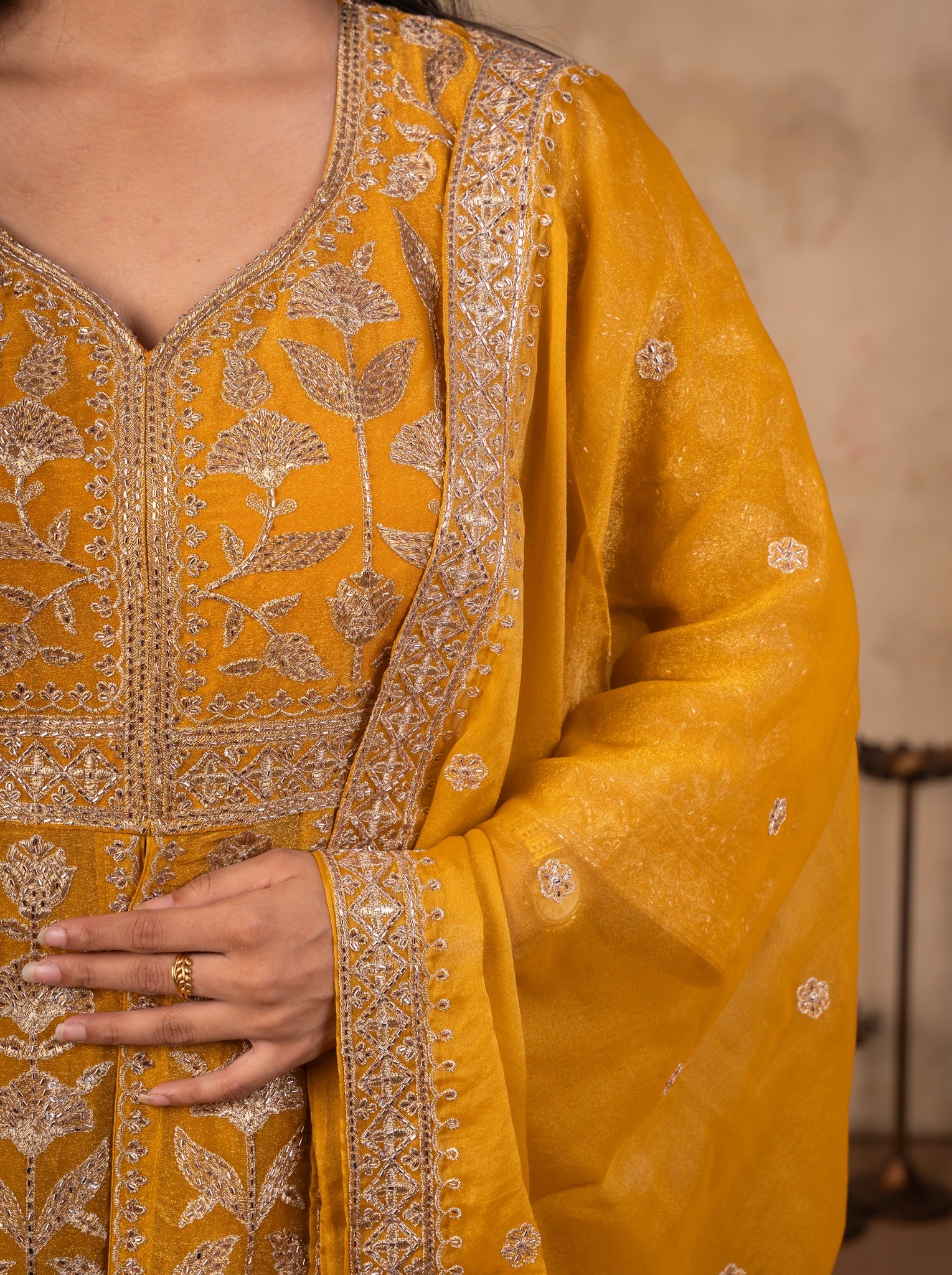 Detail of the embroidered V-neckline on a mustard tissue Anarkali and the dupatta's embellished border