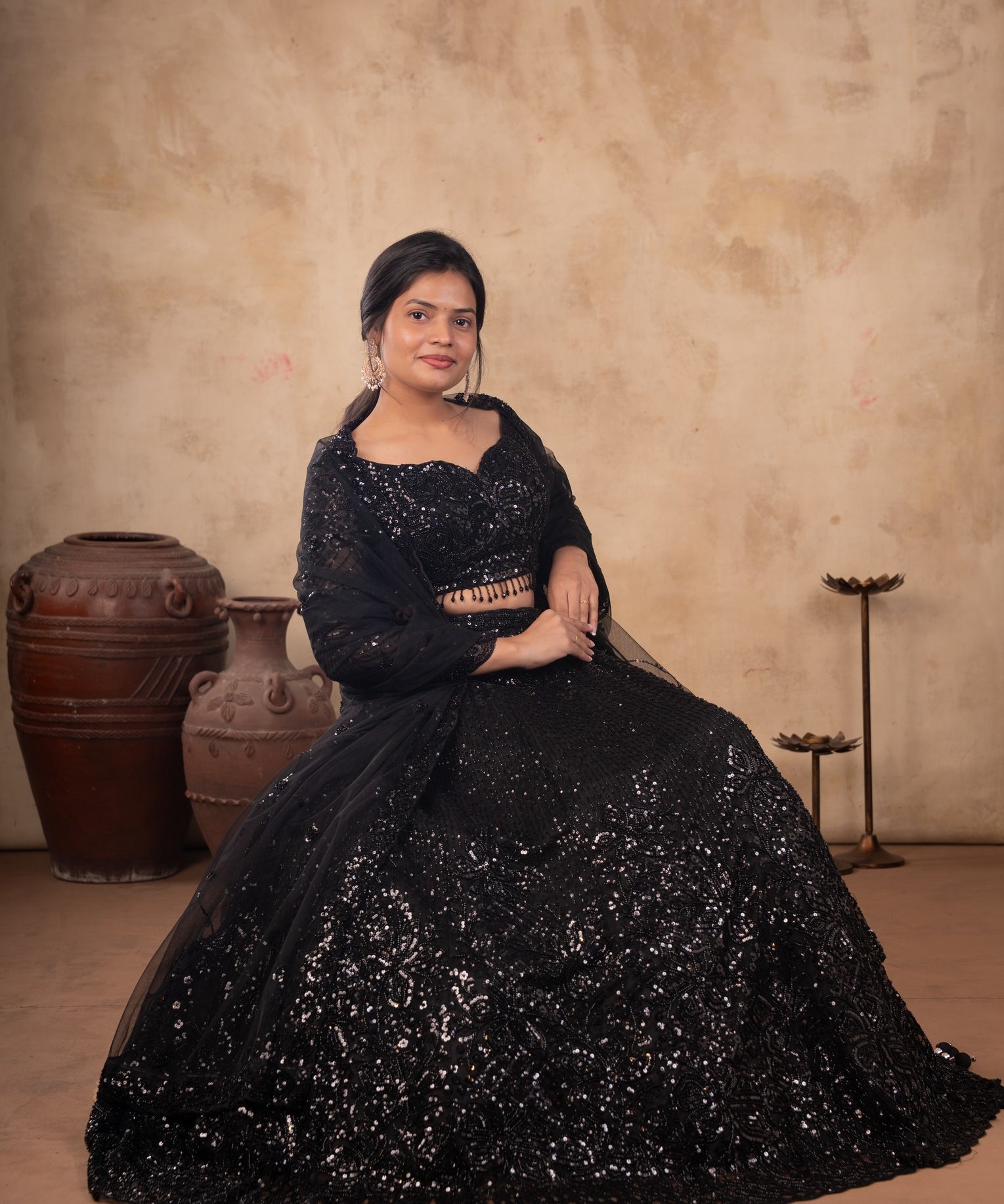 Model wearing a black net lehenga with shimmering embellishments, a matching blouse with beaded fringe, and a sheer dupatta.