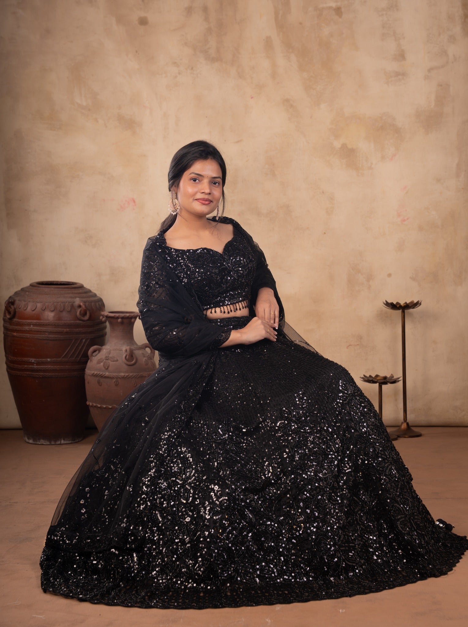 Model seated in a black net lehenga with shimmering sequin work, the flared skirt spread around her