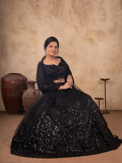 Model seated in a black net lehenga with shimmering sequin work, the flared skirt spread around her
