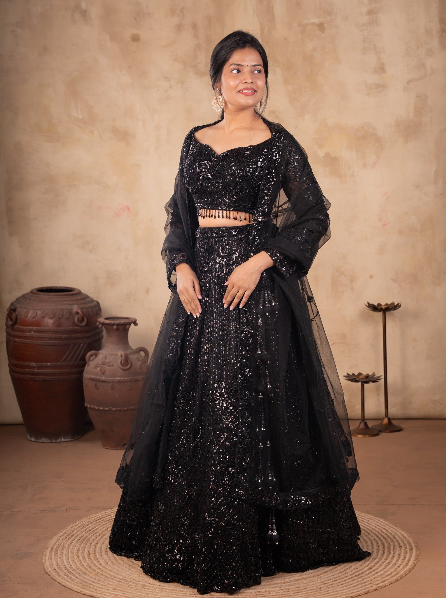 Front view of a model in a black net lehenga with sequin embellishments, a long-sleeved blouse with beaded fringe and a sheer dupatta