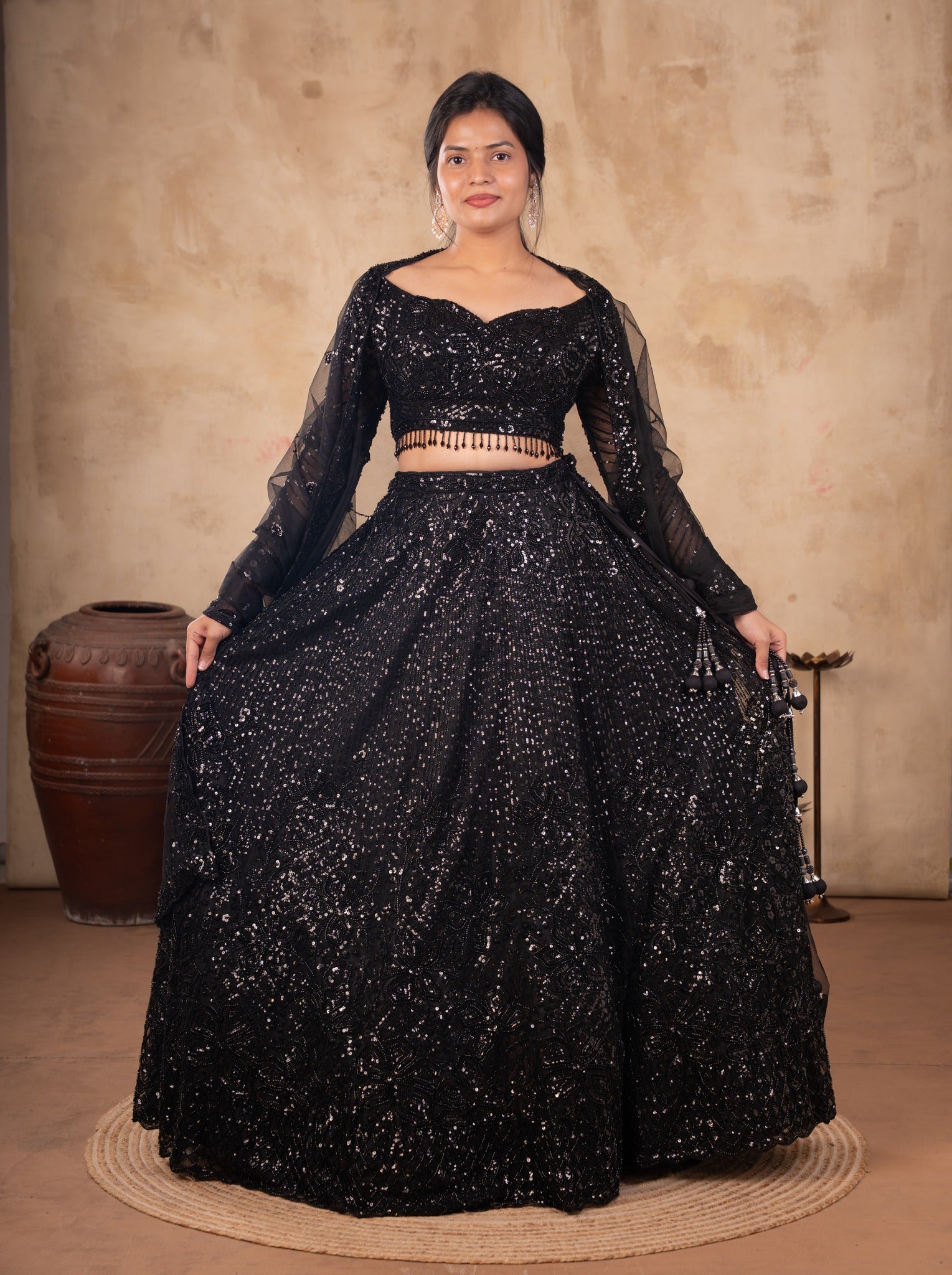 Model holding out the flared skirt of a black sequinned net lehenga with a long-sleeved blouse