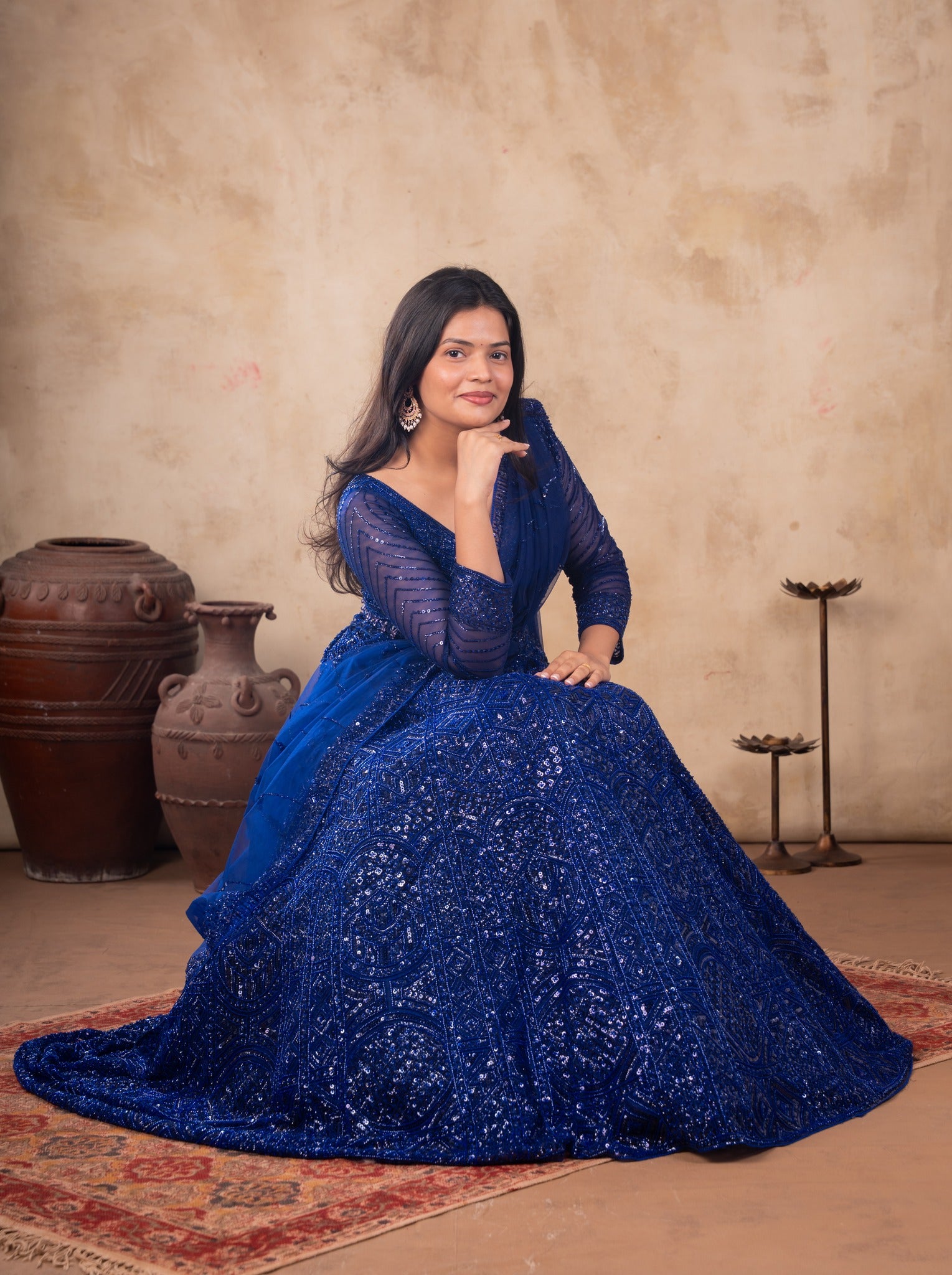 Model seated in a royal blue sequinned net lehenga with the flared skirt spread on the floor