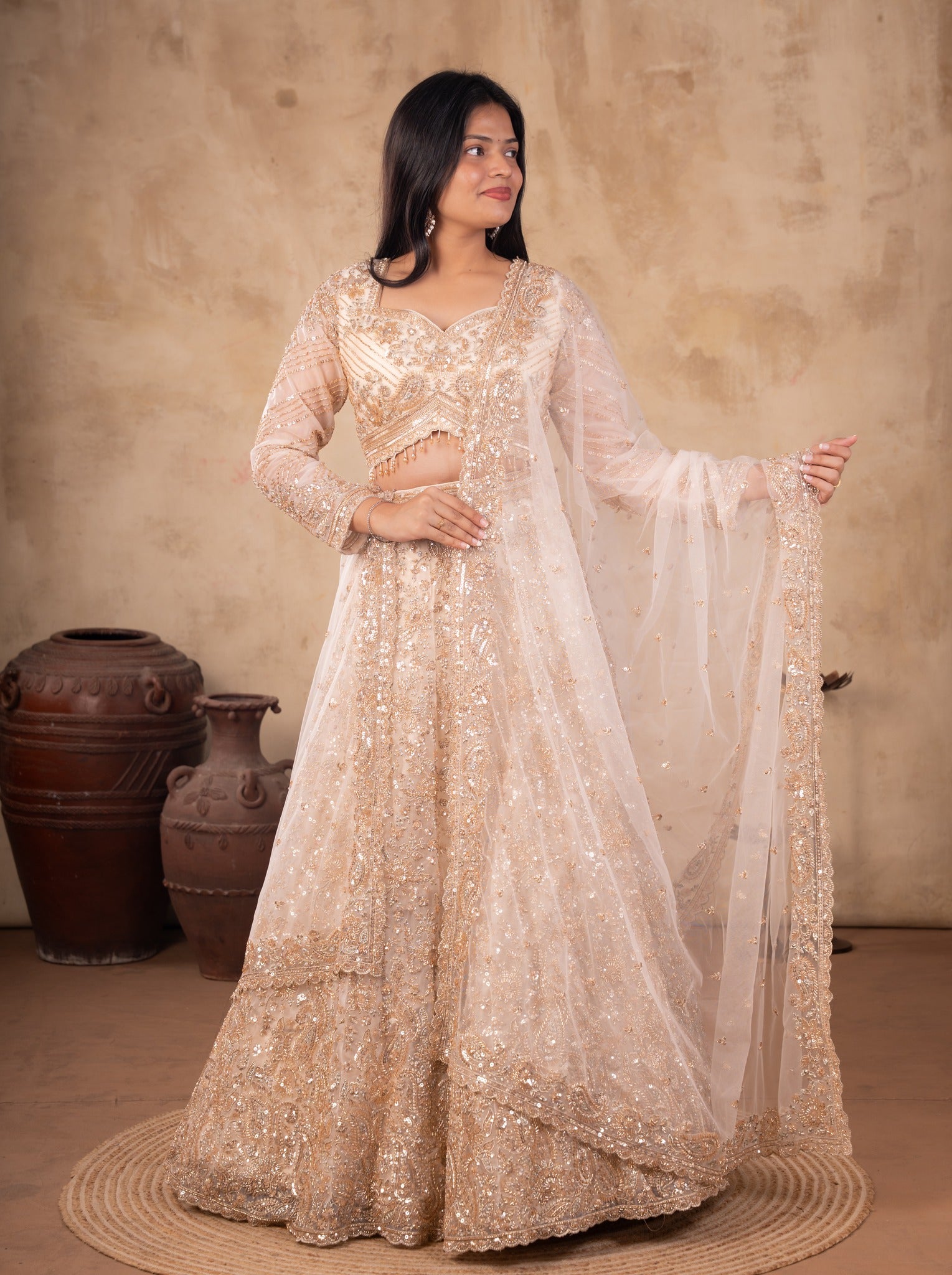 Front view of a model in a cream net lehenga with floral sequin embellishments, sheer sleeves and an embroidered dupatta