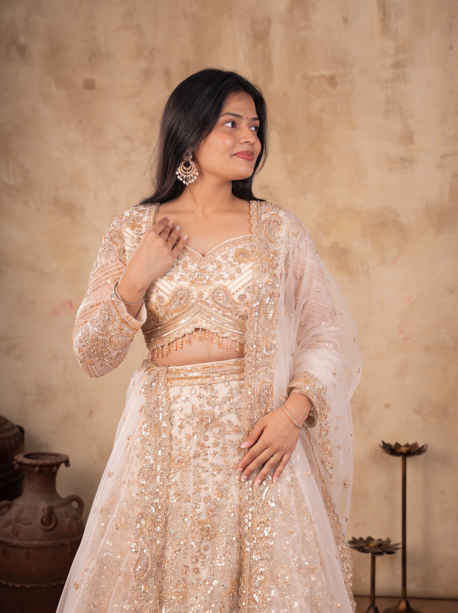 Model in a cream net lehenga with an embellished long-sleeved blouse and sheer dupatta
