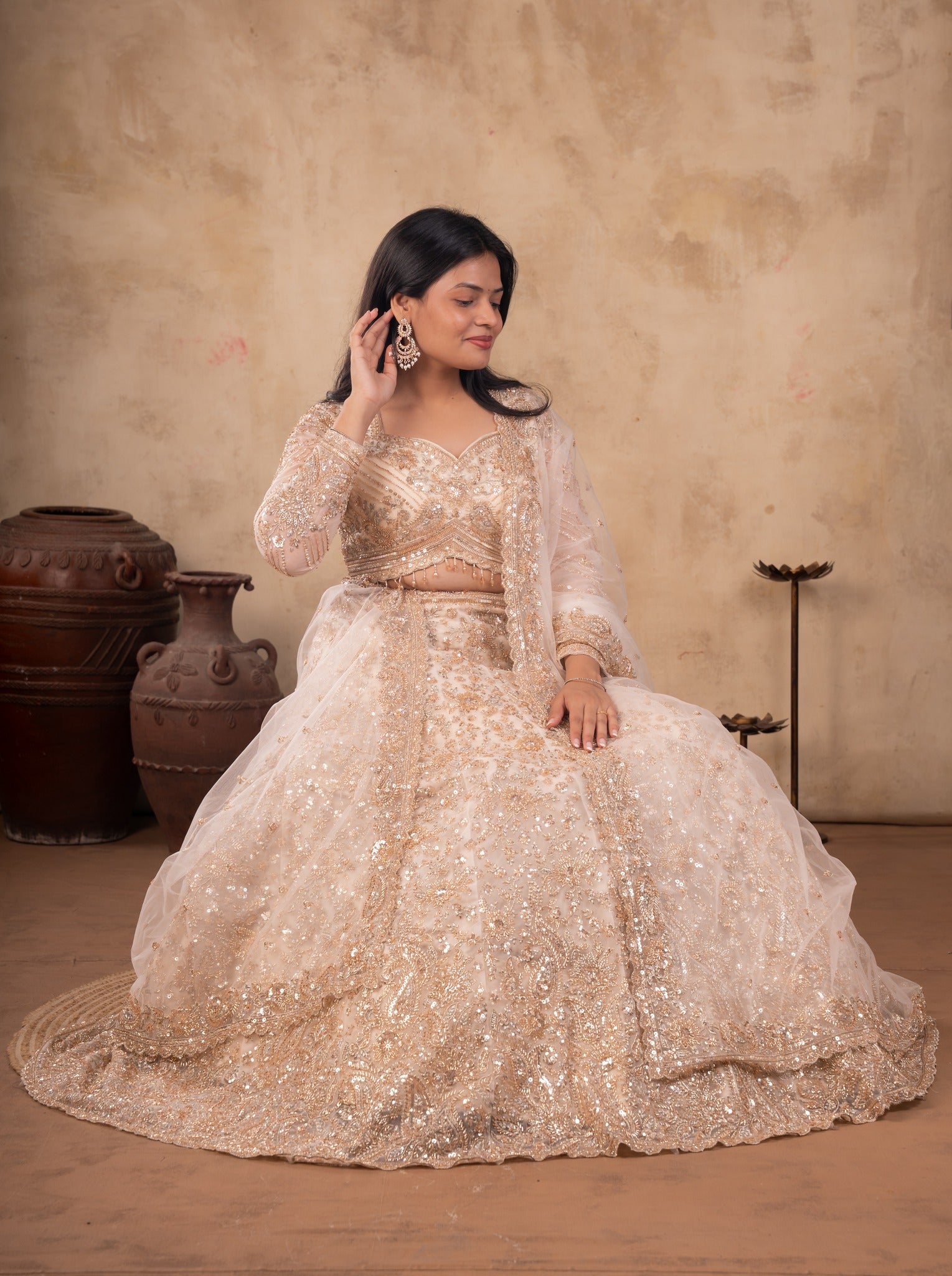 Model seated in a cream net lehenga with the embellished skirt spread around her