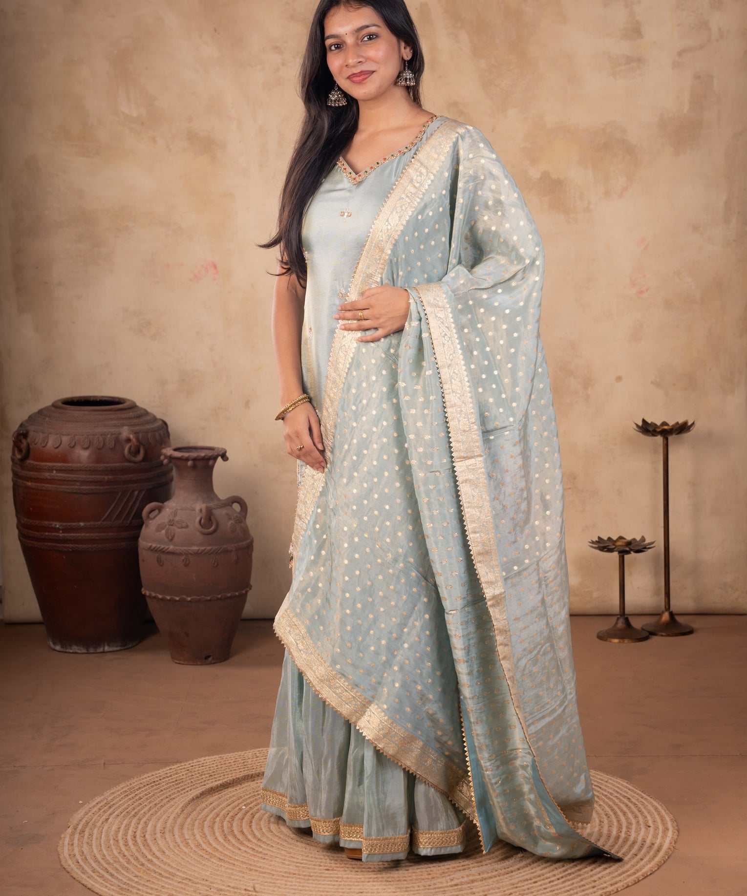 Model wearing a sea green silk salwar suit with a sleeveless embroidered kurta, flared trousers, and a dotted dupatta with a gold-toned border.
