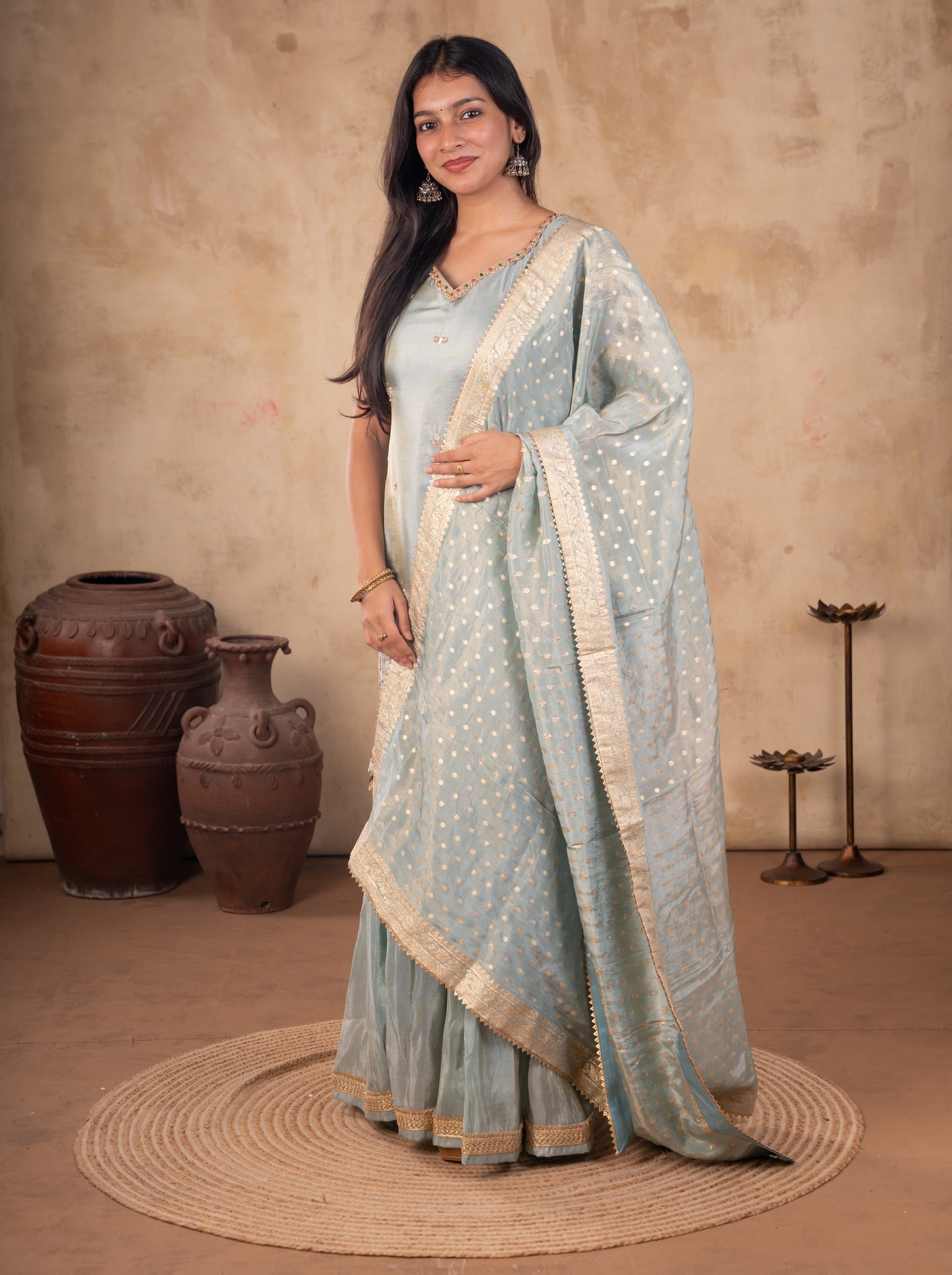 Front view of a model in a sea green silk salwar suit with a sleeveless embroidered kurta, flared trousers and a dotted dupatta with a gold border