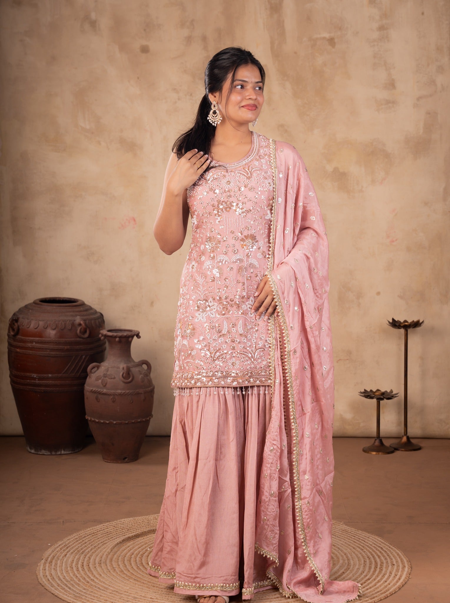 Front view of a model in a peach silk salwar suit with an embroidered kurta, flared sharara trousers and a dotted dupatta