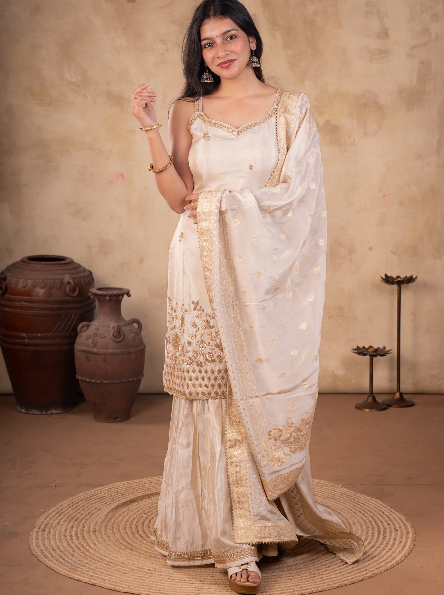 Front view of a model in a white silk salwar suit with a strappy floral-embroidered kurta, flared trousers and a gold-bordered dupatta