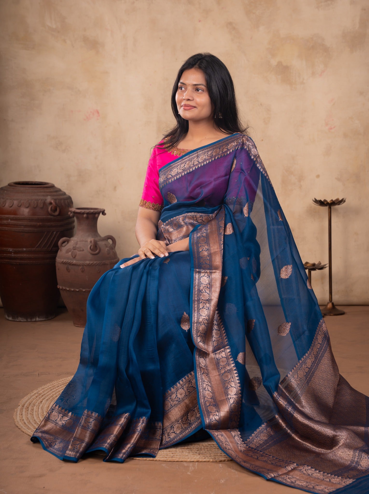 Model seated in a blue Banarasi silk saree with metallic woven motifs and a bright pink blouse