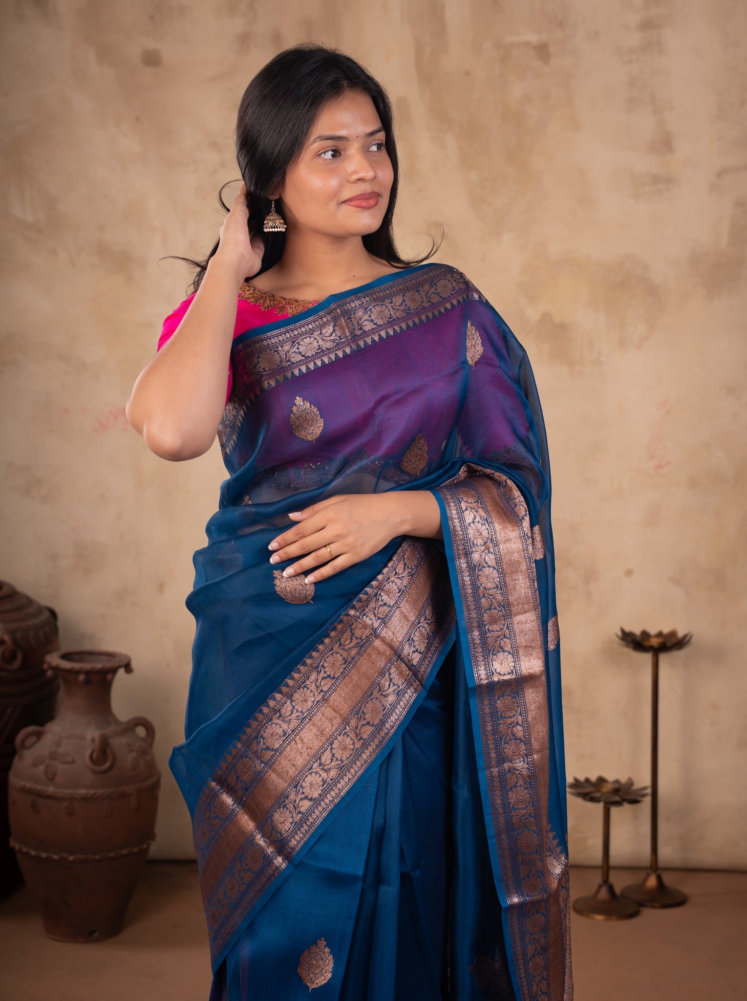 Model holding the pallu of a blue Banarasi silk saree with a broad metallic border and a pink blouse