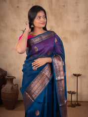 Model holding the pallu of a blue Banarasi silk saree with a broad metallic border and a pink blouse