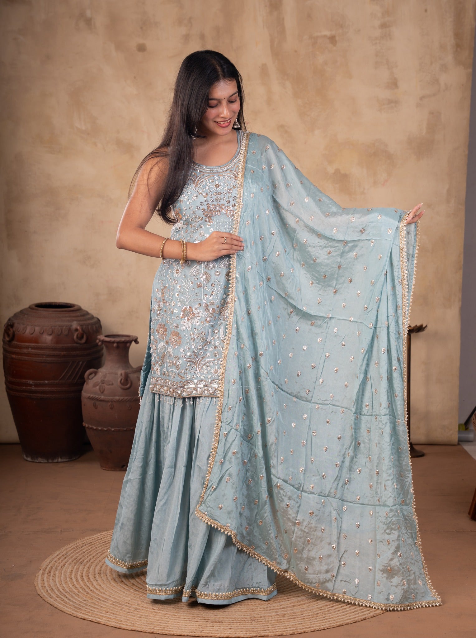 Front view of a model in a sage green georgette sharara suit with a floral-embroidered kurta and a dupatta held out