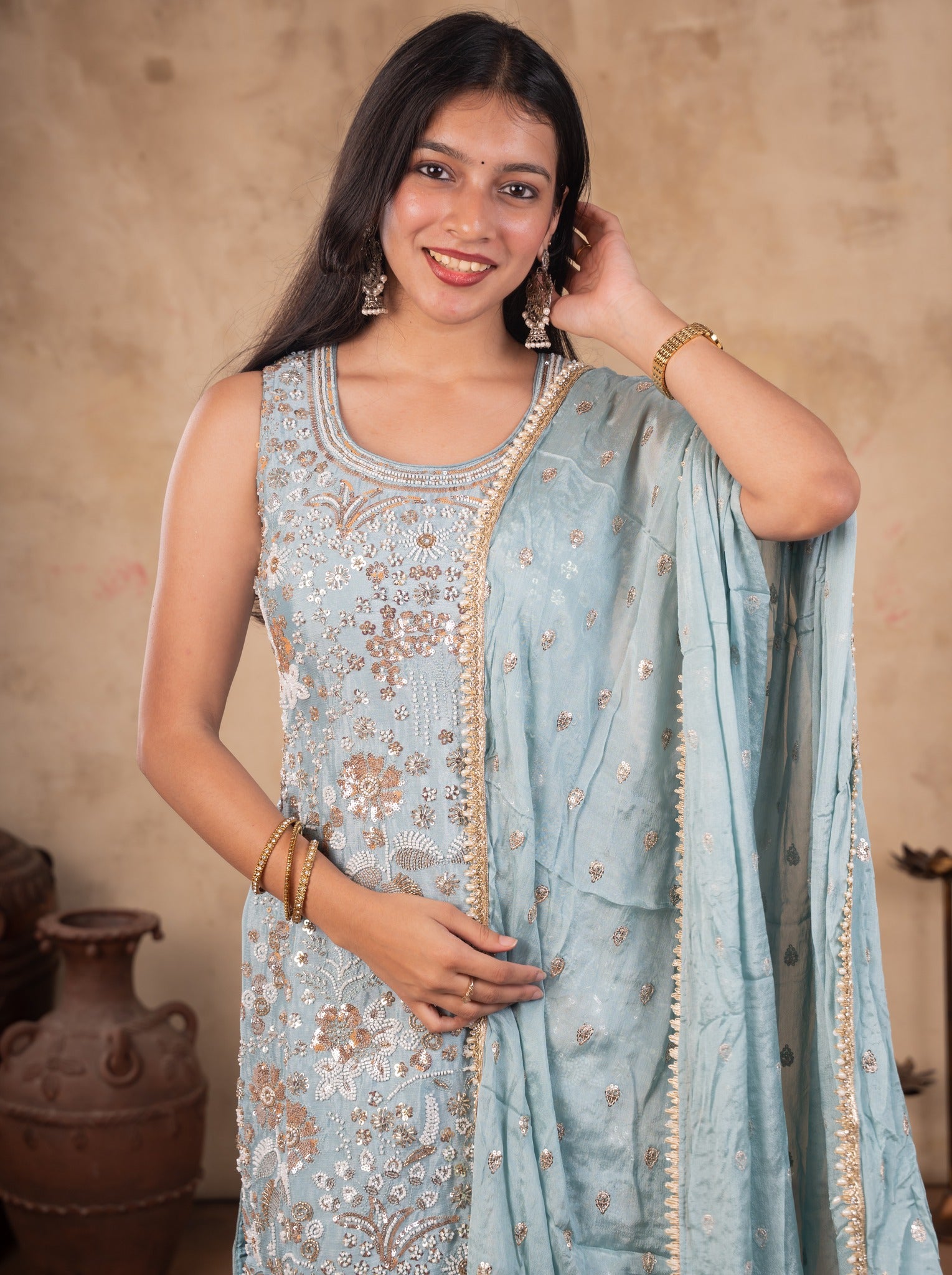 Model smiling in a sage green georgette sharara suit with an embroidered sleeveless kurta and matching dupatta