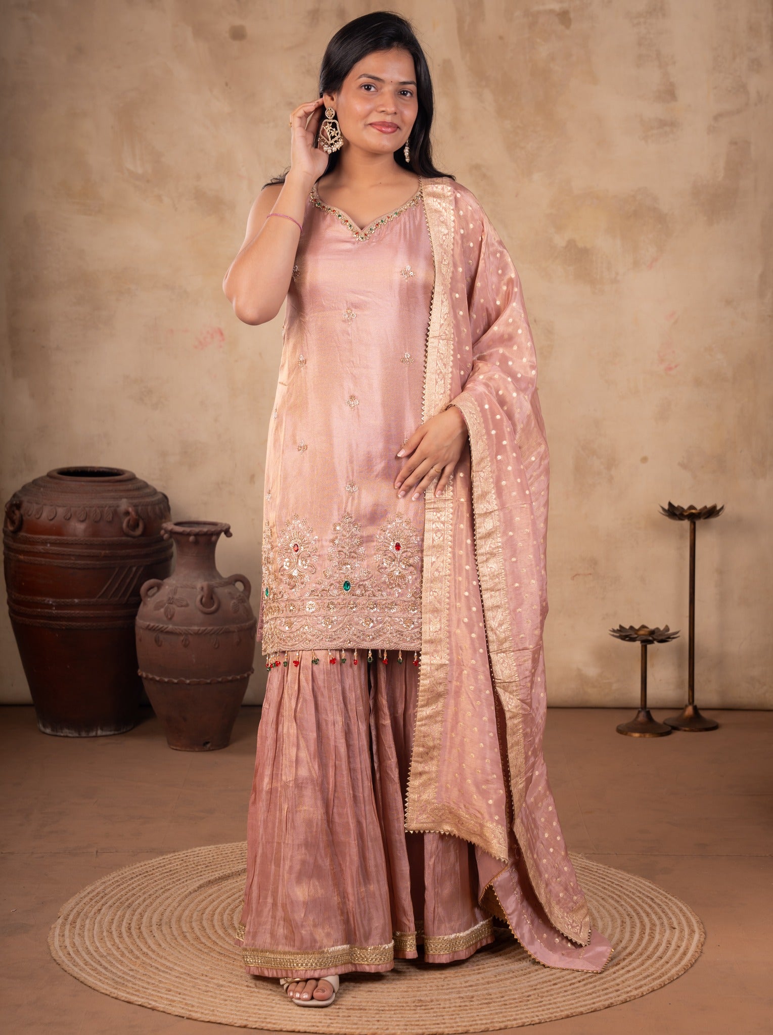 Front view of a model in a blush pink georgette sharara suit with an embroidered kurta and dupatta with a lace border