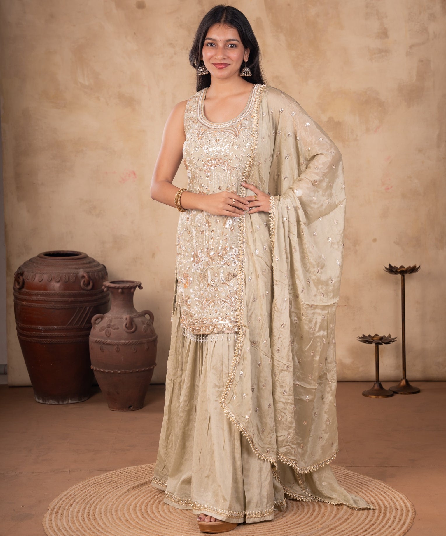 Model wearing a light olive green georgette sharara suit with a floral-embellished kurta, flared trousers, and a matching dupatta with decorative trim.