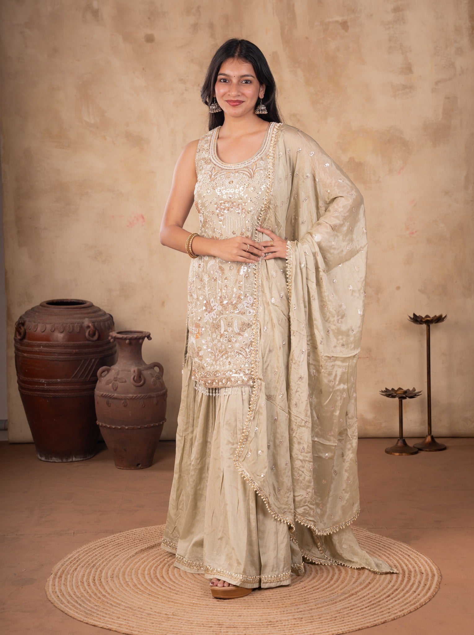Front view of a model in a light olive green georgette sharara suit with a floral-embellished kurta and matching dupatta