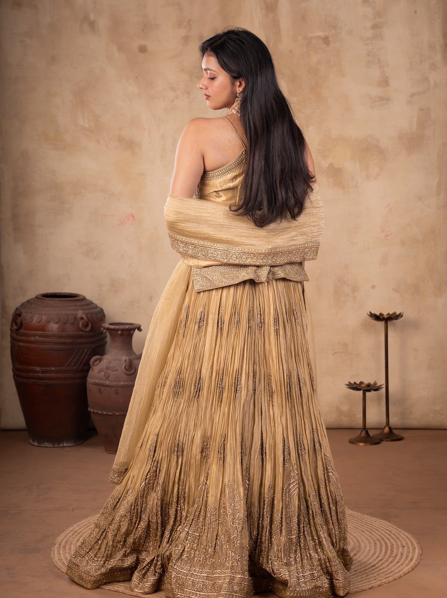 Back view of a model in a pista organza lehenga with a pleated embroidered skirt and a sheer dupatta draped across her arms