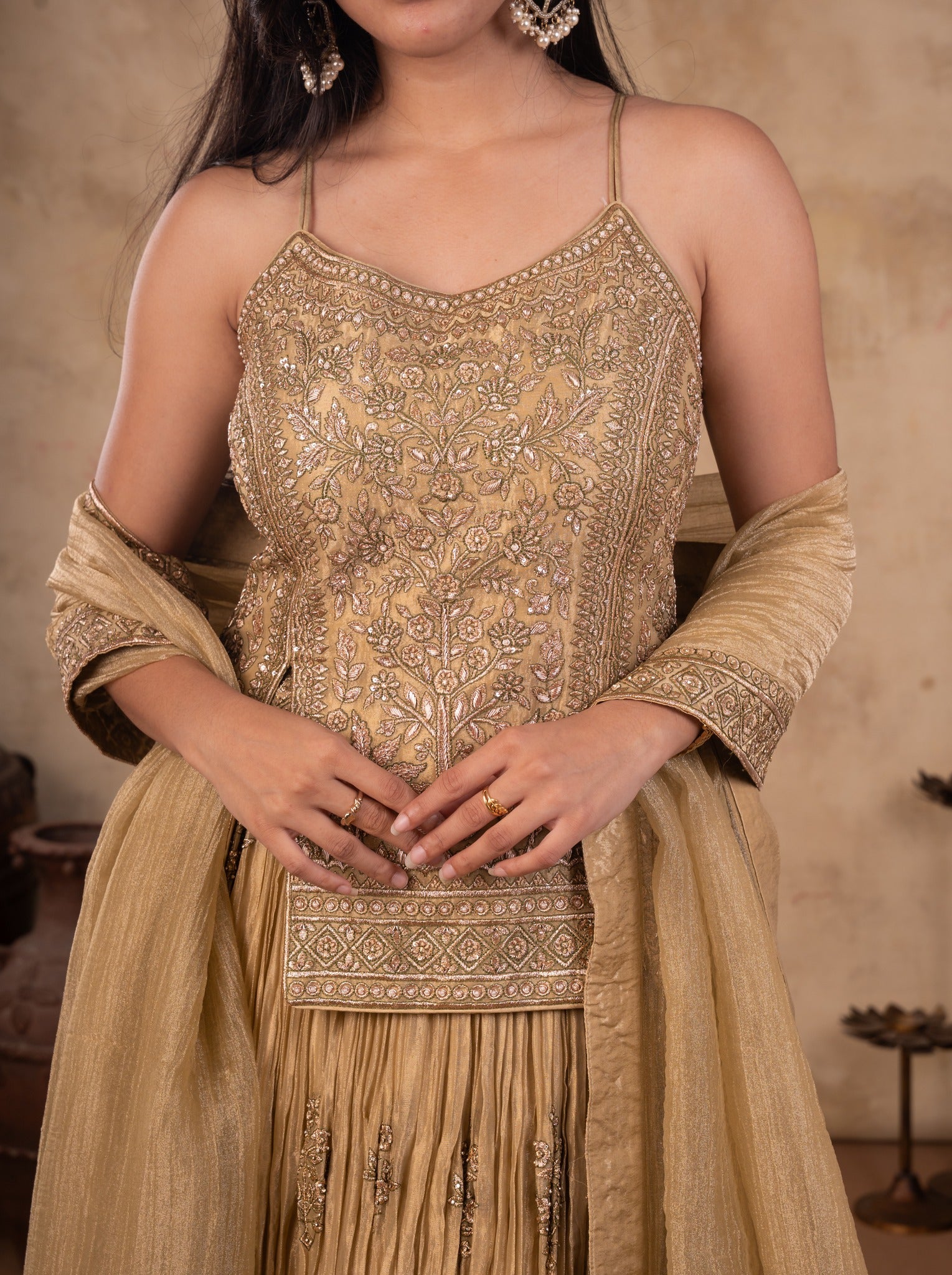 Close-up of the embroidered strappy choli on a pista organza lehenga with the dupatta over her arms