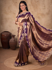 Model holding out the patterned pallu of a bronze-toned saree with a deep purple border