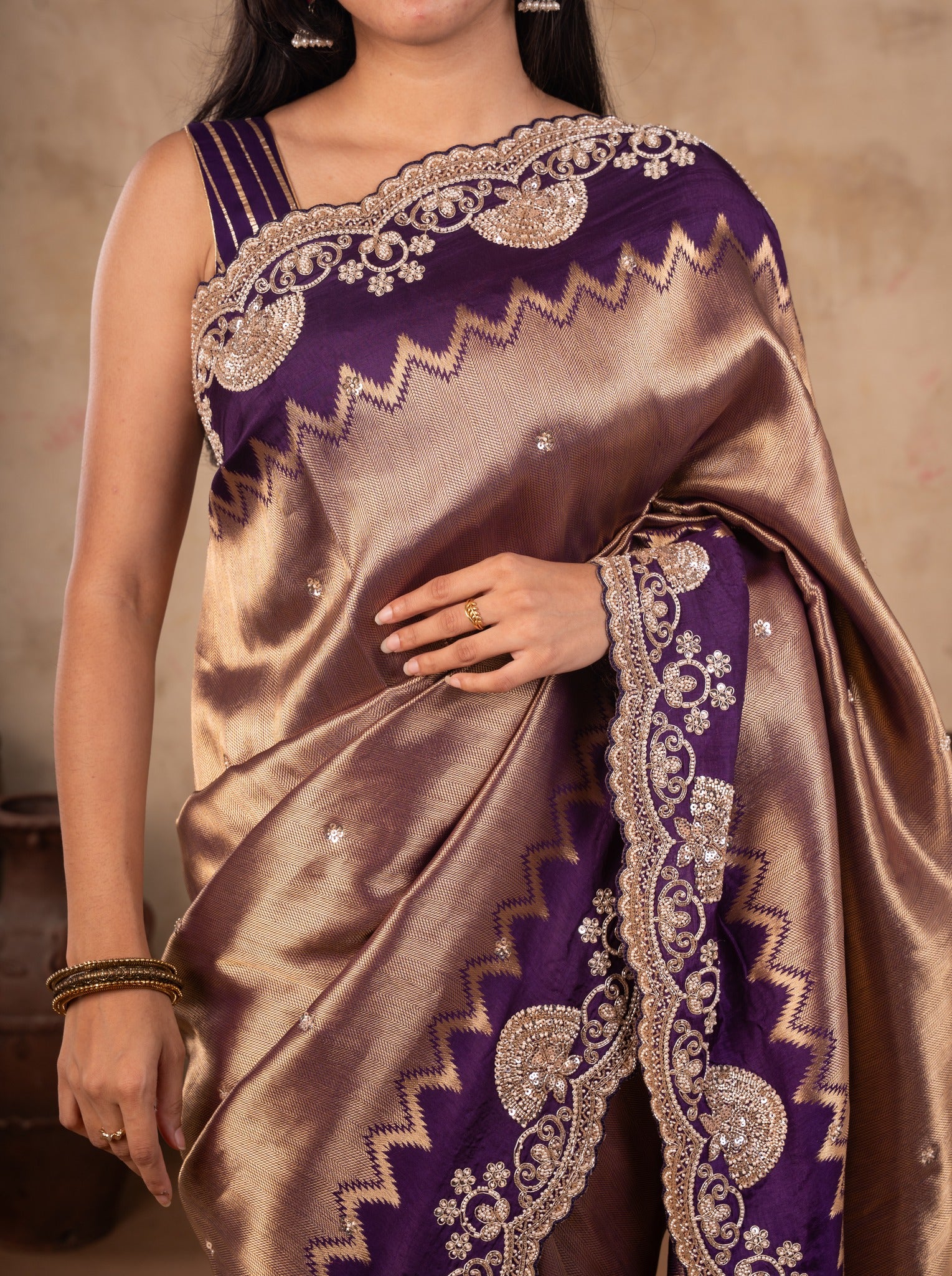 Close-up of the deep purple border with gold floral and zigzag embellishment on a bronze-toned saree