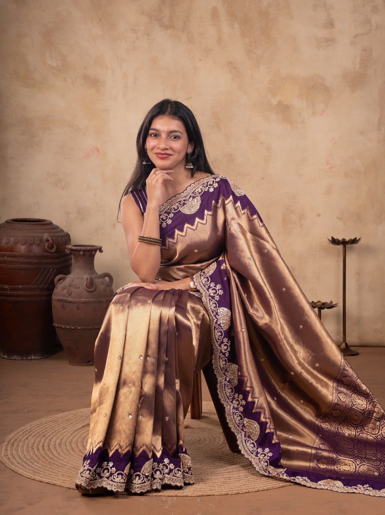 Model seated in a bronze-toned saree with a purple embellished border, the pallu spread on the floor