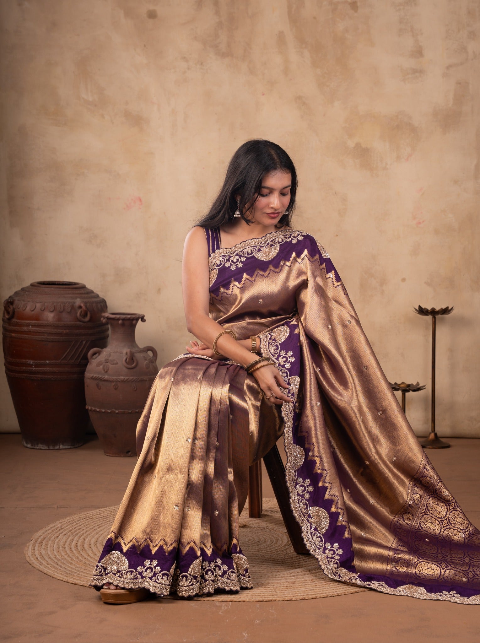 Seated pose in a lustrous bronze-toned saree with ornate purple border