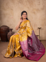 Model seated in a mustard soft silk saree with a contrast pink and silver woven pallu