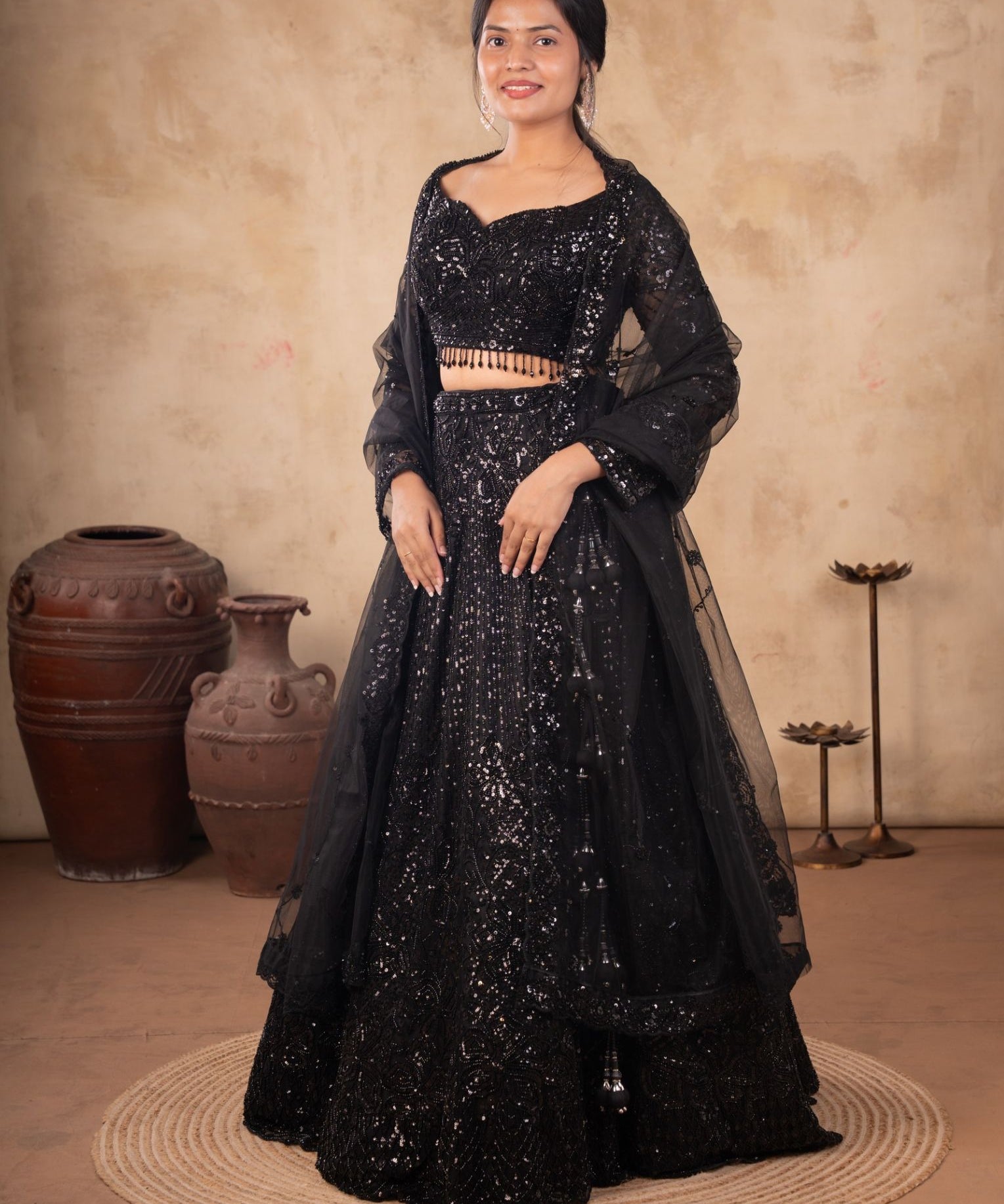 Model wearing a black net lehenga with shimmering embellishments, a matching blouse with beaded fringe, and a sheer dupatta.