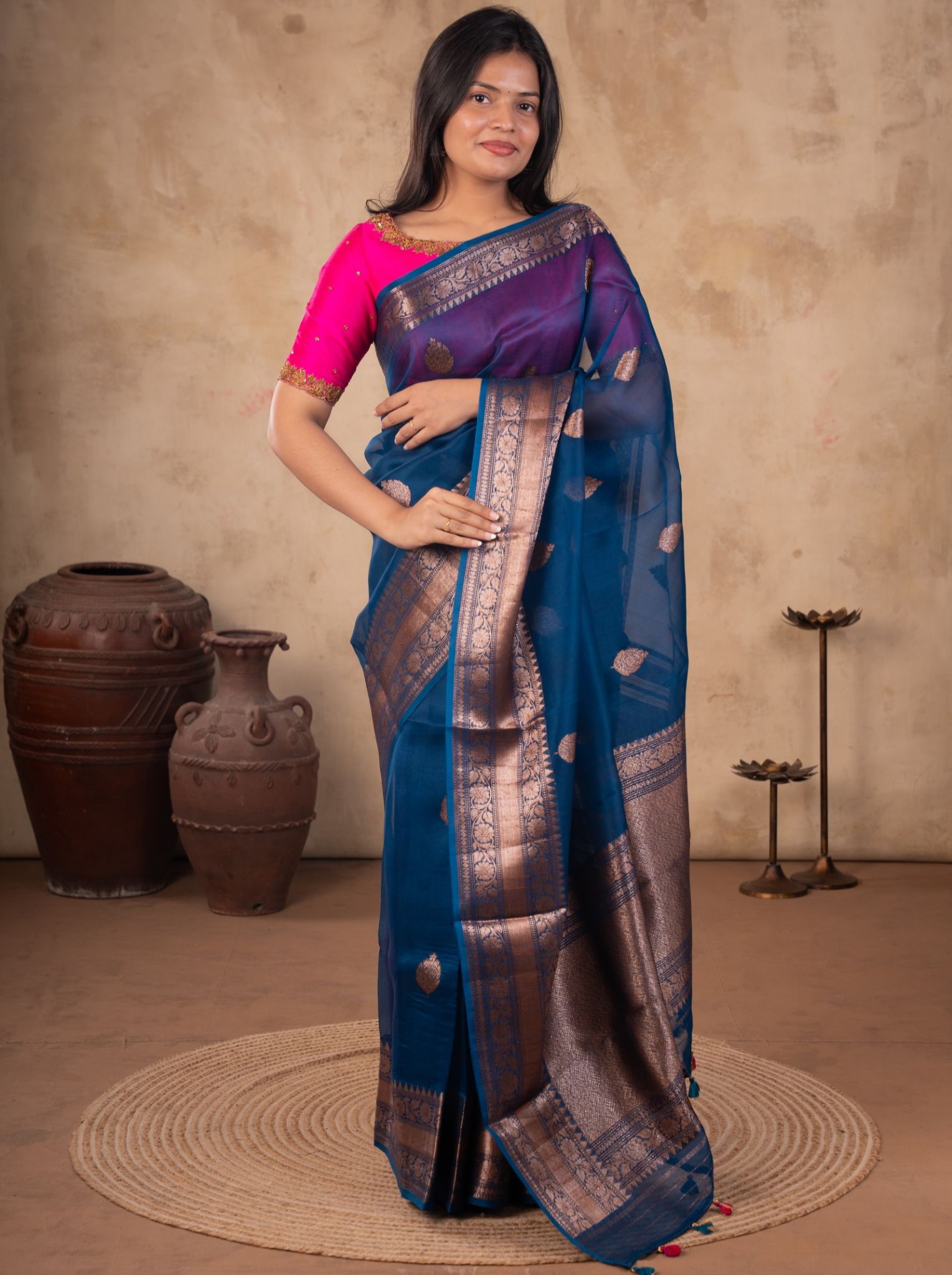 Model wearing a blue Banarasi silk saree with metallic woven motifs, an ornate broad border and pallu, paired with a bright pink blouse.
