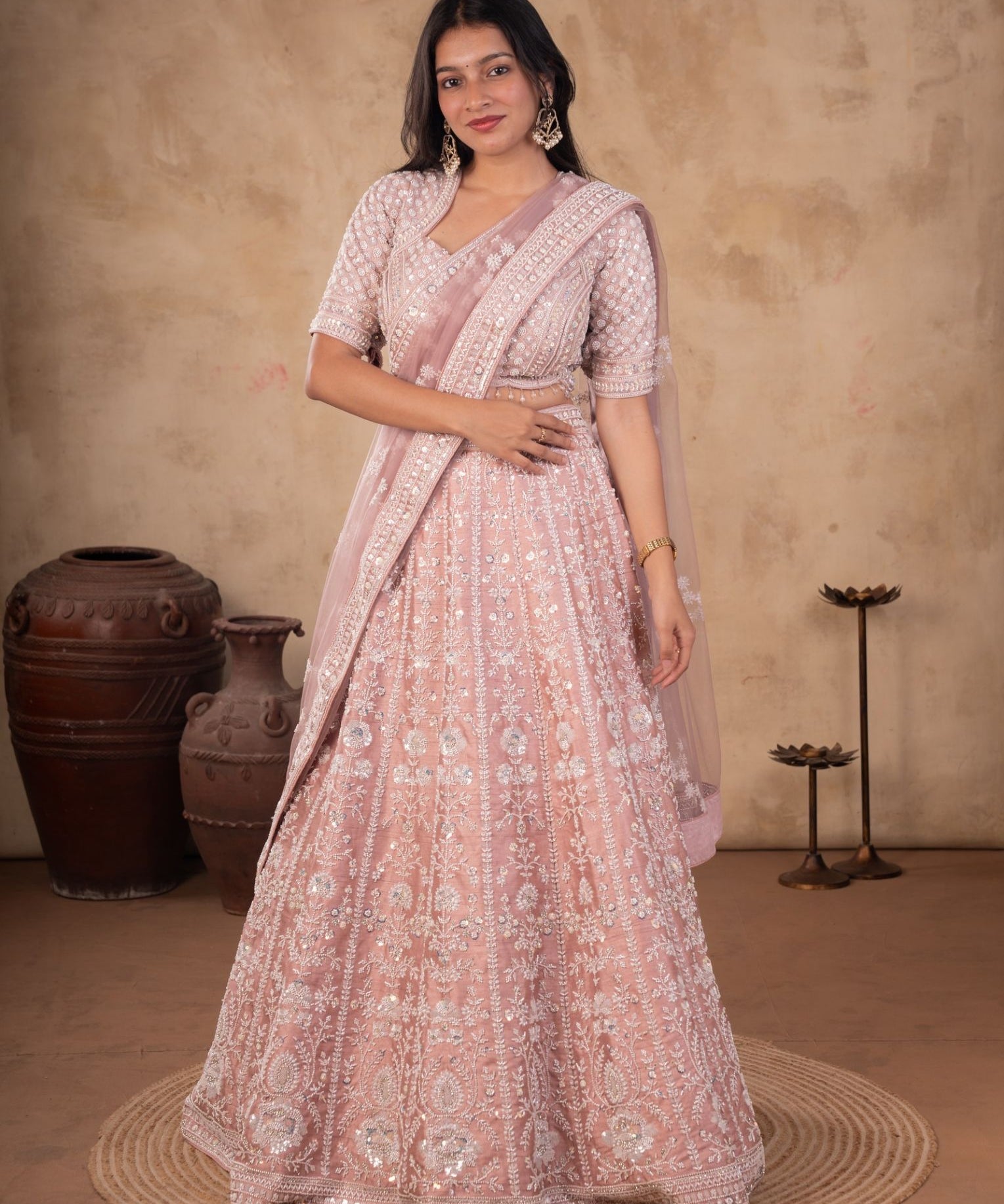 Woman wearing a blush pink net lehenga with silver sequin and thread embroidery, a stitched V-neck blouse and a matching net dupatta draped over one shoulder
