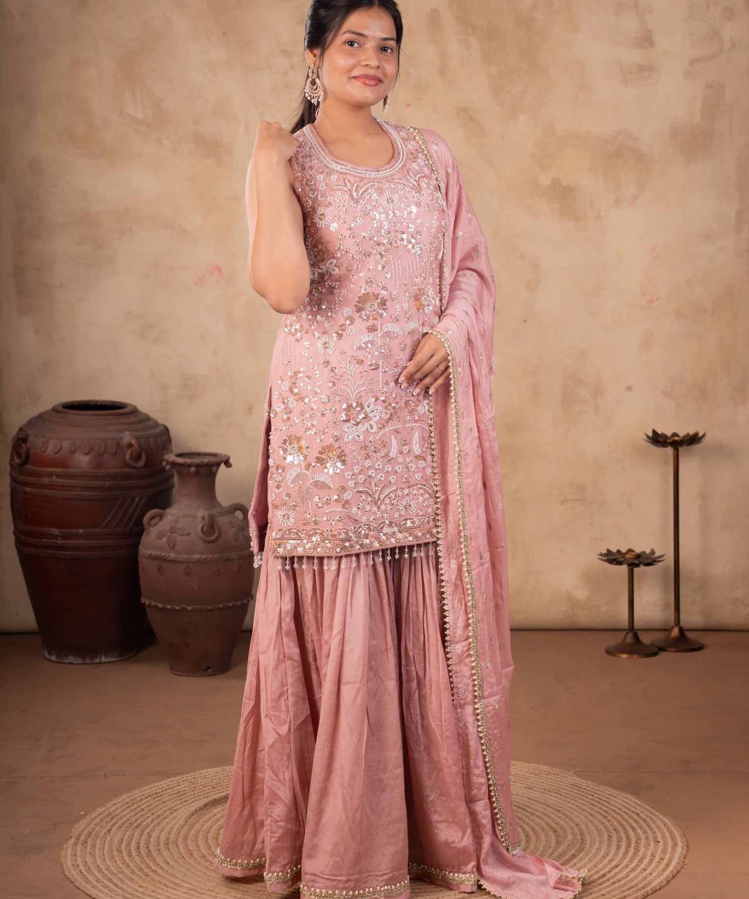 Woman wearing a blush pink georgette sharara suit set with a sequin-embroidered kurta, flared sharara and a dupatta with a beaded lace border