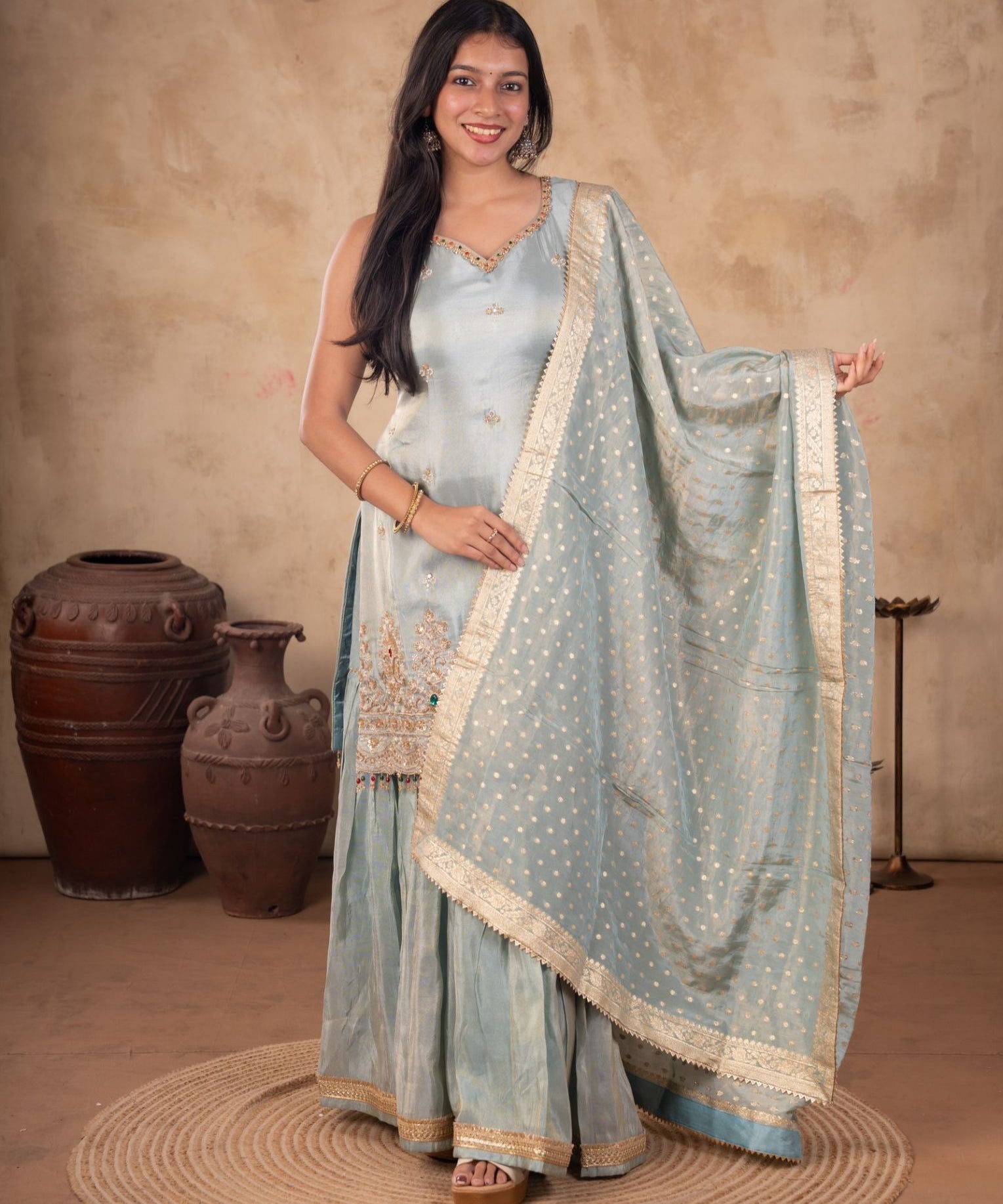 Model wearing a sea green silk salwar suit with a sleeveless embroidered kurta, flared trousers, and a dotted dupatta with a gold-toned border.